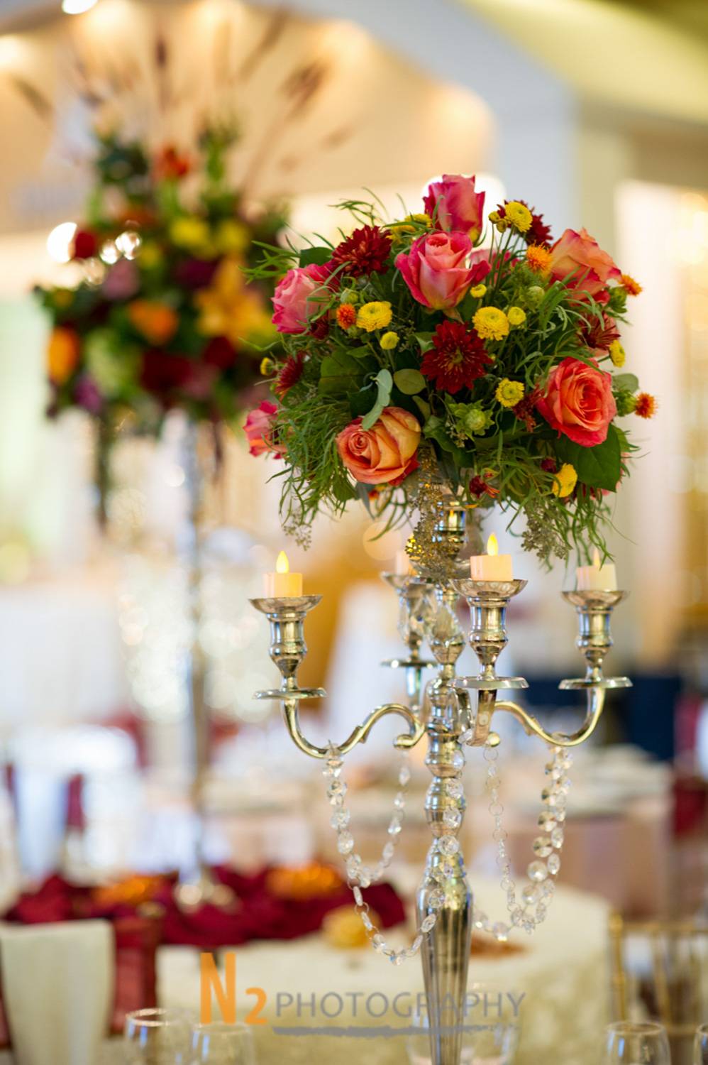 Luxurious floral arrangement with vibrant roses and chrysanthemums atop a silver candelabra centerpiece, highlighting Alegria Gardens’ precision in event decor.