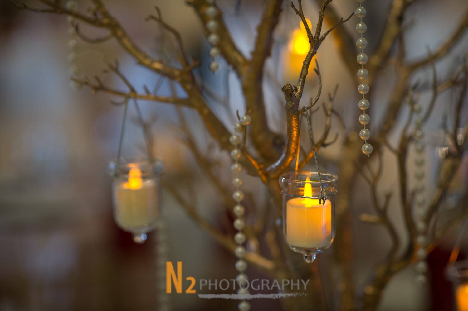 Close-up of hanging candle decorations and pearl strands on a rustic branch centerpiece, reflecting the refined ambiance created by Alegria Gardens.
